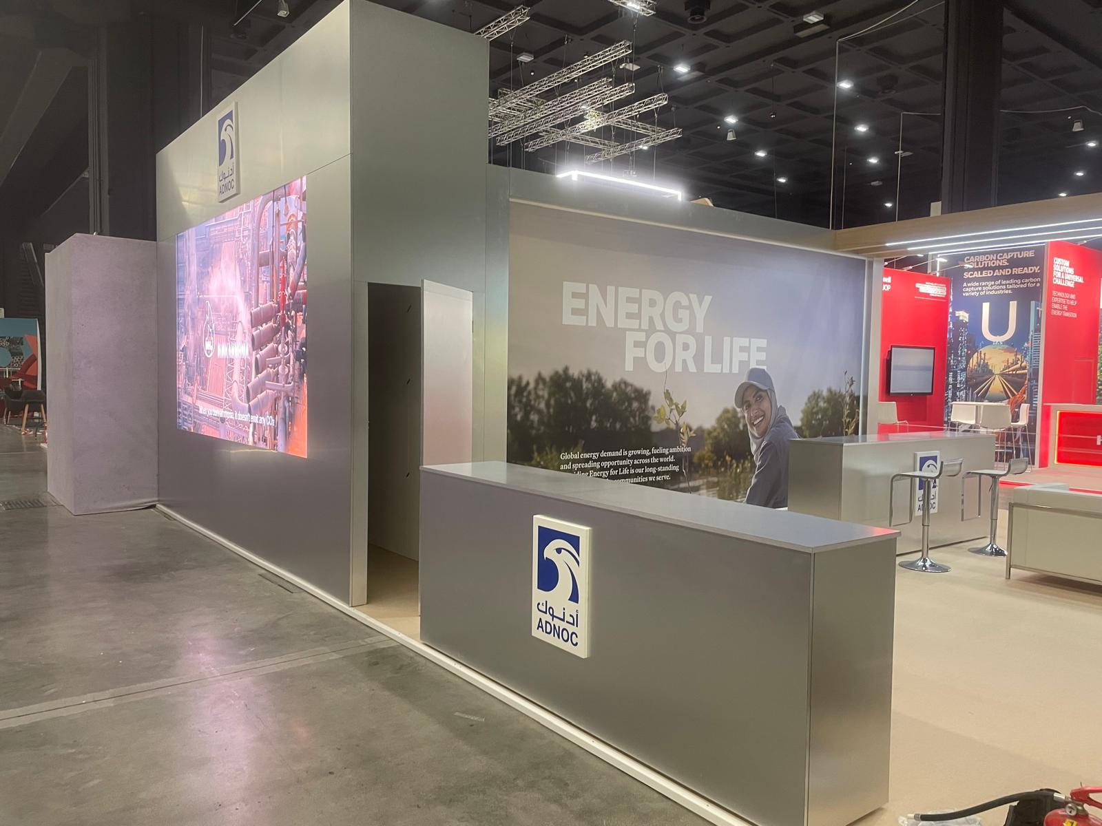 Stand ADNOC con schermi, grafica Energy for Life e banconi grigi